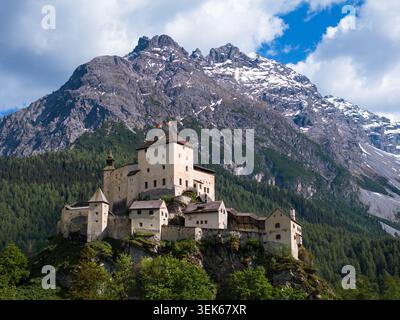 Vista aerea dello Schloss Tarasp, un castello medievale arroccato su una collina rocciosa circondato da lussureggianti foreste verdi e torreggianti vette alpine a Scuol, Graubund Foto Stock