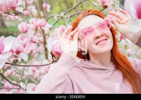 Donna di mezza età dai capelli rossi con occhiali a forma di cuore rosa quasi rosa Foto Stock