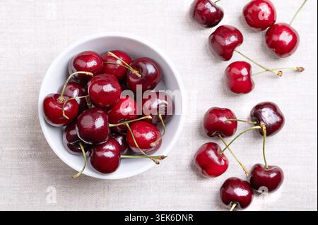 Ciliegie fresche in una ciotola bianca su lino. Pronti da mangiare, frutti rossi e maturi della vera specie di ciliegio Prunus avium, un frutto di pietra. Foto Stock