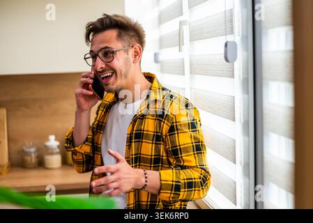 Un giovane allegro parla al telefono cellulare a casa. Foto Stock