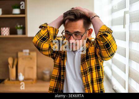 Nel profondo del pensiero, un giovane uomo in piedi nella sua cucina, che sembra sopraffatto dallo stress o da notizie inaspettate. Foto Stock