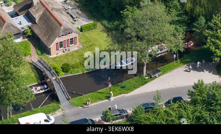 Vista aerea di una tradizionale casa con tetto in paglia accanto a uno stretto canale con turisti in piccole barche e un ponte pedonale in legno a Giethoorn, Overijssel, Foto Stock