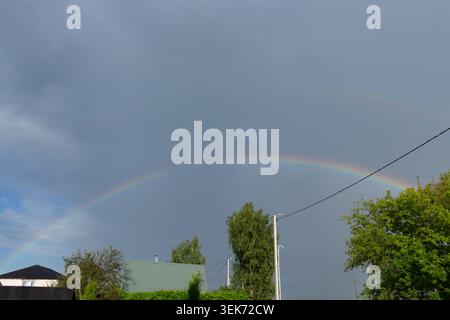 Doppio arcobaleno nel cielo buio e tempestoso dopo la pioggia. Paesaggio di campagna con alberi verdi Foto Stock