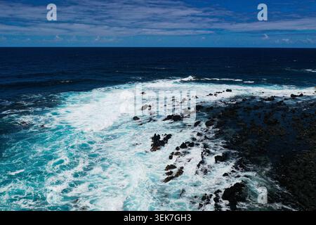 Una fotografia aerea che cattura la splendida costa rocciosa di Maui, Hawaii, con acque turchesi che si schiantano contro le rocce vulcaniche nere sotto un p Foto Stock