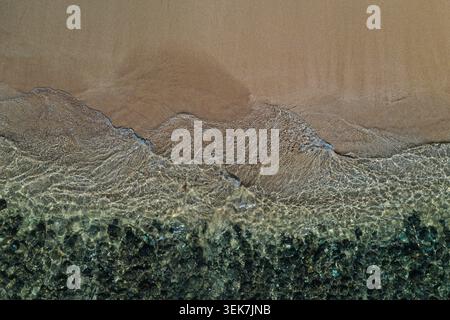 Una prospettiva aerea che cattura una spiaggia di sabbia incontaminata con acque turchesi limpide che lambiscono dolcemente sulla costa di Maui, Hawaii. Texture vivaci di Foto Stock