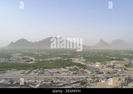 La città di Kandahar si estende attraverso una vibrante valle verde, circondata da aspre montagne in una giornata nebulosa Foto Stock
