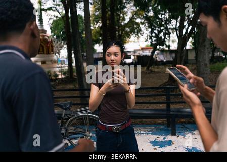 Giovane donna che si concentra sul telefono cellulare, persone che interagiscono digitalmente in un parco Foto Stock