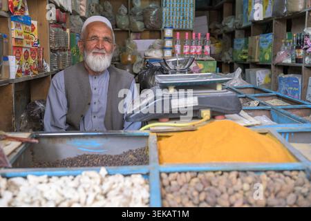 Sorridente afghano con barba bianca che lavora nel suo tradizionale negozio di spezie, vendendo varie spezie e merci. Foto Stock