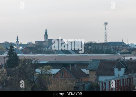 Soffice foschia mattutina su una tranquilla cittadina europea, che mette in risalto le alture della chiesa, i tetti a strati e l'architettura mista suburbana; l'atmosfera tranquilla trasmette Foto Stock