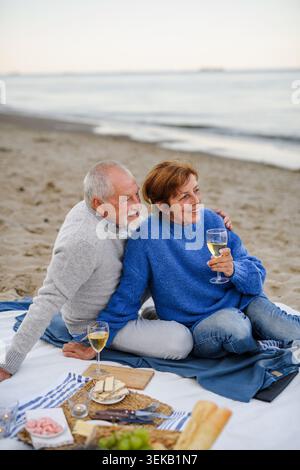 Una coppia di anziani innamorati per un romantico picnic sulla spiaggia in riva al mare. Foto Stock