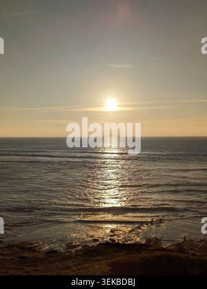 La luce del sole dorata si riflette sull'Oceano Pacifico, vista da una vista costiera al tramonto. Tranquillo paesaggio marino con acqua scintillante. Foto Stock