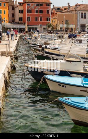 Piccole barche attraccavano al porto di Rovigno nel centro storico dell'Istria, in Croazia, con pedoni lungo la banchina di pietra in una giornata di sole. Foto Stock