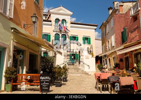 Caffetteria all'aperto con edifici colorati e l'edificio del Circolo su scale di pietra a Rovigno, Croazia. Foto Stock