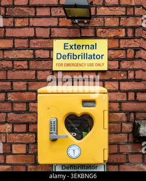 Scatola defibrillatore esterna della vecchia scuola di Donacarney, County Meath, Irlanda, montata su una parete di mattoni rossi con segnaletica di emergenza sopra di essa. Foto Stock