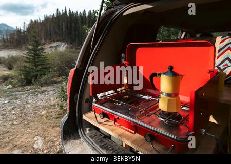 vista sul retro di un camper con una stufa rossa e una macchina per caffè espresso gialla in estate al mattino Foto Stock