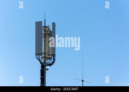 Vista ravvicinata dell'antenna di una stazione base cellulare sopra il tetto di un edificio con cielo limpido, che mostra le apparecchiature di comunicazione wireless e l'infrazione della rete urbana Foto Stock