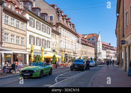 Bamberga, Baviera, Germania - 7 aprile 2026: Le persone si siedono ai tavoli mentre le auto passano su Lange Strasse Foto Stock