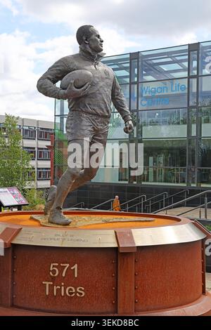 571 tentativi Statua di Billy Boston nel centro della città di Wigan, Greater Manchester, Inghilterra, Regno Unito, vista più ampia con il Wigan Life Centre. RIP Sir Bill 24/08/2026 Foto Stock