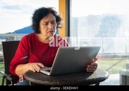 Donna matura che lavora al computer all'aperto su una terrazza soleggiata Foto Stock