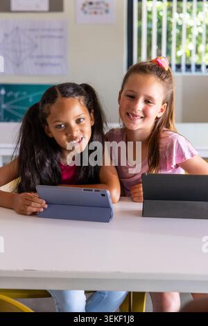 Diverse studentesse di classe di bambini sedute al tavolo della classe utilizzando tablet con coperture grigie e nere Foto Stock