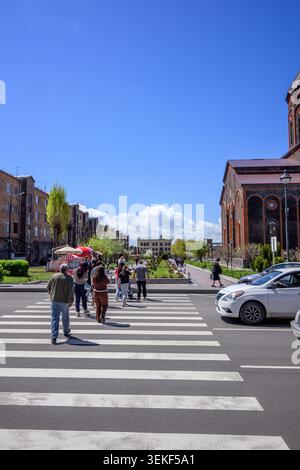 I pedoni attraversano la strada all'incrocio vicino alla chiesa. Auto parcheggiate accanto alla strada Foto Stock