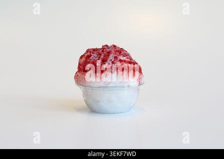 Dessert con ghiaccio rasato ai mirtilli rossi in un recipiente di plastica trasparente su sfondo bianco con sciroppo e gocciolatoio cremoso Foto Stock