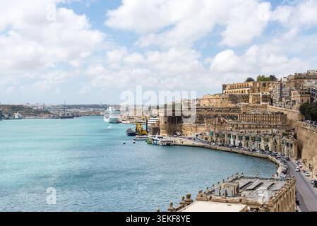 La Valletta, Malta - 16 maggio 2025: Il Bastione di Santa Barbara si affaccia sul turchese Grand Harbour con le storiche mura di pietra, la nave da crociera e le fortificazioni costiere Foto Stock