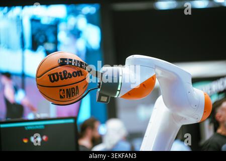 Un braccio robotico collaborativo bianco e arancione utilizza una pinza meccanica specializzata per tenere un basket NBA ufficiale durante un demonio della tecnologia Foto Stock