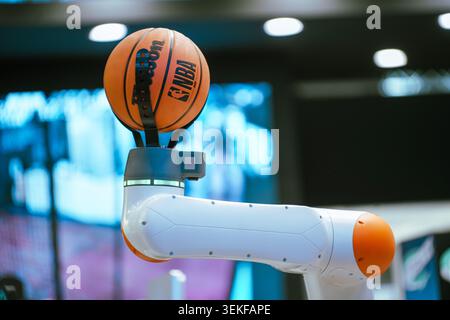 Un braccio robotico collaborativo bianco e arancione utilizza una pinza meccanica specializzata per tenere un basket NBA ufficiale durante un demonio della tecnologia Foto Stock