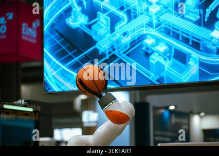 Un braccio robotico collaborativo bianco e arancione utilizza una pinza meccanica specializzata per tenere un basket NBA ufficiale durante un demonio della tecnologia Foto Stock