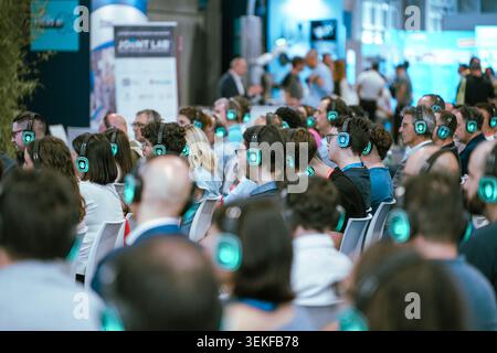 Il pubblico indossa cuffie wireless luminose durante una conferenza silenziosa in occasione di una fiera dedicata alla tecnologia e all'innovazione industriale. Foto Stock