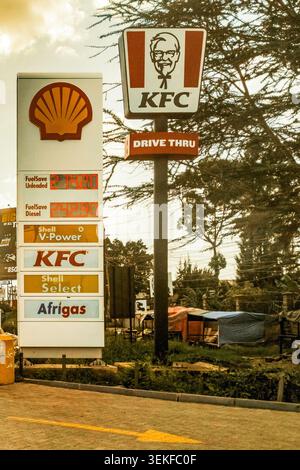 Syokimau, Kenya - 18 maggio 2026: Un totem per stazione di servizio Shell che mostra i prezzi del carburante accanto a un cartello KFC Drive Thru su una striscia commerciale a lato della strada. Foto Stock