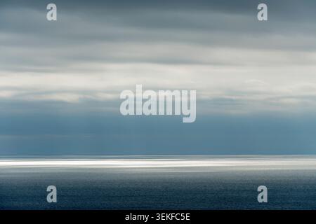 LA LUCE DEL SOLE SPLENDE ATTRAVERSO UNA COPERTA DI NUVOLE DI STRATUS SUL MARE Foto Stock