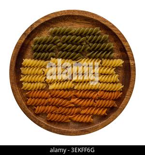 Fusilli tricolori disposti in file ordinate su un piatto di legno visto dall'alto su sfondo bianco. Foto Stock