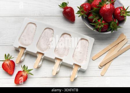 Preparare i papaveri di yogurt alla fragola in una muffa di silicone con frutta fresca e bastoncini di legno Foto Stock