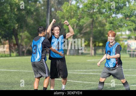 I giocatori di calcio multietnico celebrano la vittoria in squadra su un campo all'aperto, indossando maglie blu e mostrando emozioni dopo una partita. La squadra l'ha fatto Foto Stock
