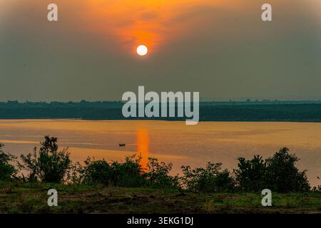 Il sole dorato sorge sul lago Mboro, in Uganda, gettando un caldo riflesso sull'acqua con una piccola barca che naviga nel tranquillo paesaggio mattutino e nel dist Foto Stock
