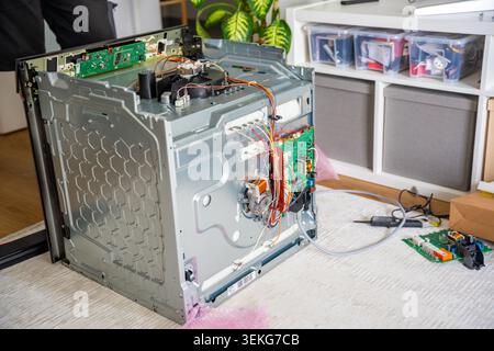 Area di lavoro per la riparazione di elettrodomestici con forno elettrico smontato e parti elettroniche di ricambio. Concetto di servizio professionale Foto Stock