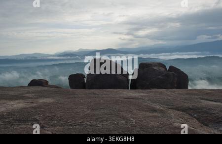 Un tranquillo paesaggio caratterizzato da grandi massi scuri in primo piano che si affaccia su una vallata vasta e nebbiosa. Colline ondulate e catene montuose svaniscono nel Foto Stock