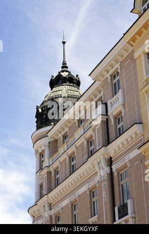 Classico edificio europeo con una facciata in pietra ornata, finestre multiple, cupola angolare e guglia appuntita che si innalzano su un cielo blu limpido, che mostra h Foto Stock