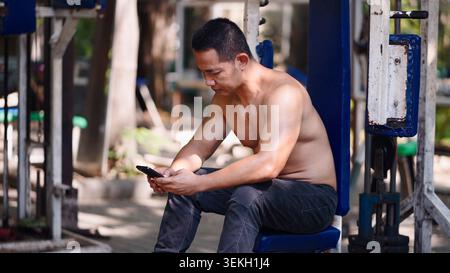 Uomo che controlla il telefono nella vecchia palestra all'aperto, si prende una pausa dalla sessione di allenamento Foto Stock