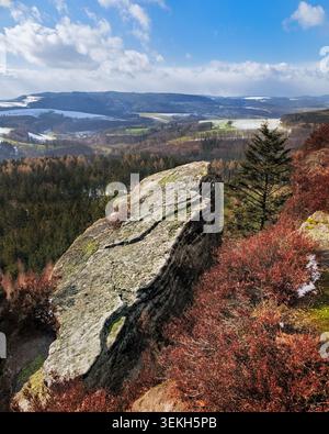 Grande roccia in primo piano con cespugli aridi e una valle lontana spolverata di neve Foto Stock
