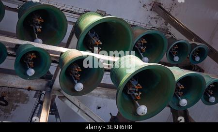Le campane di carillon verde con i clappers bianchi sono appese a una struttura metallica. La ruggine è visibile sul metallo. Alcune campane presentano motivi decorativi. Colon leggero Foto Stock