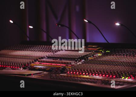 Console di missaggio audio in uno studio di registrazione poco illuminato, con manopole di controllo illuminate, fader e indicatori LED con profondità di campo ridotta Foto Stock