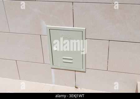 Una cassetta di servizio in metallo verde chiaro con la parola GAS in rilievo è montata su una parete piastrellata beige, fornendo accesso a un misuratore Foto Stock