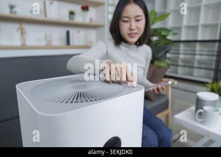 Una donna interagisce con un purificatore d'aria in un elegante soggiorno, mostrando i moderni elettrodomestici e la gestione della qualità dell'aria Foto Stock
