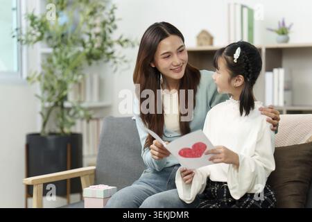 Una madre e una figlia condividono un momento di amore insieme, scambiandosi una carta fatta a mano e godendosi lo spirito delle vacanze Foto Stock