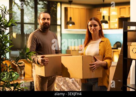 Ritratti di coppia, spostandosi in una nuova casa, con scatole di cartone, proprietà di casa. Uomo e donna felici che si sentono orgogliosi degli investimenti immobiliari e si godono un nuovo inizio insieme, un evento di vita. Foto Stock