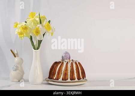 Concetto di festa pasquale, torta pasquale tradizionale, statuette di coniglietto pasquale e narcisi primaverili in un vaso su un elegante sfondo di cucina, Pasqua di Foto Stock