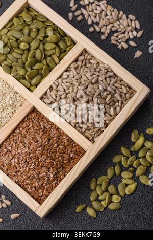 Una scatola di lino, zucca, girasole e semi di sesamo, ingredienti per una sana alimentazione. Semi di lino, sesamo, zucca e girasole come sfondo alimentare f Foto Stock